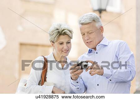 Stock Photography - Smiling middle-aged couple reviewing photos on digital camera outdoors. Fotosearch