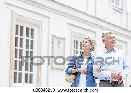 Stock Image - Smiling middle-aged couple standing with arm in arm outside building. Fotosearch