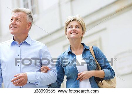 Stock Photography - Smiling middle-aged couple standing with arm in arm outdoors. Fotosearch