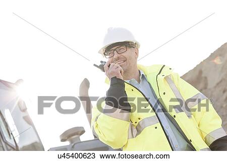 Smiling supervisor using walkie-talkie at construction site against clear sky View Large Photo Image Stock Image - Smiling supervisor using walkie-talkie at construction site against clear sky. Fotosearch