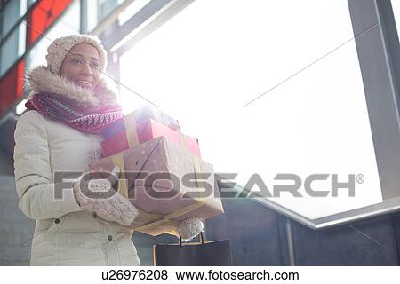 Smiling woman in warm clothing carrying stacked gifts by window View Large Photo Image Stock Photo - Smiling woman in warm clothing carrying stacked gifts by window. Fotosearch