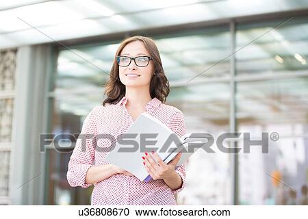 Smiling woman looking away while holding outside building View Large Photo Image Stock Image - Smiling woman looking away while holding outside building. Fotosearch