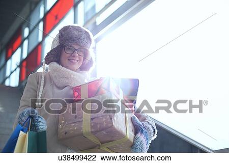 Smiling woman with stacked gifts and shopping standing by window during winter View Large Photo Image Stock Image - Smiling woman with stacked gifts and shopping standing by window during winter. Fotosearch