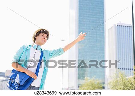 Smiling young man hailing a taxi in city View Large Photo Image Stock Photo - Smiling young man hailing a taxi in city. Fotosearch