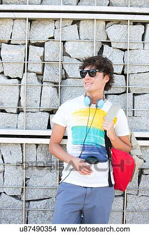 Smiling young man looking away while standing against stone wall View Large Photo Image Picture - Smiling young man looking away while standing against stone wall. Fotosearch