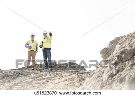 Stock Image - Supervisor discussing with colleague at construction site against clear sky. Fotosearch