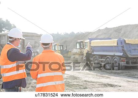 Picture - Supervisor explaining plan to colleague at construction site. Fotosearch