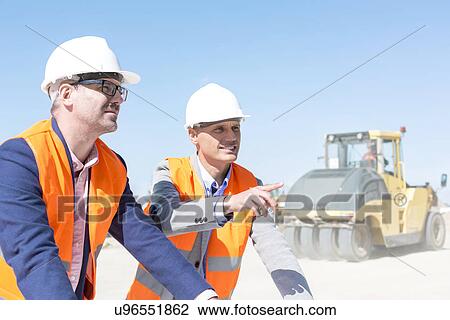 Stock Image - Supervisor explaining plan to colleague at construction site against clear sky. Fotosearch