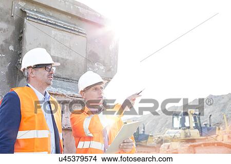 Picture - Supervisor showing something to colleague at construction site on sunny day. Fotosearch