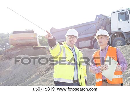 Supervisor showing something to colleague while discussing at construction site View Large Photo Image Stock Photo - Supervisor showing something to colleague while discussing at construction site. Fotosearch