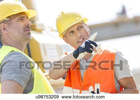 Stock Photo - Supervisor showing something to colleague at construction site on sunny day. Fotosearch