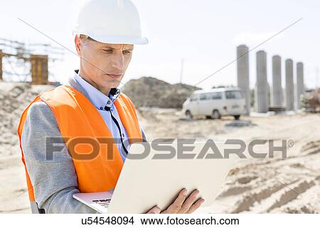 Supervisor using laptop at construction site on sunny day View Large Photo Image Picture - Supervisor using laptop at construction site on sunny day. Fotosearch