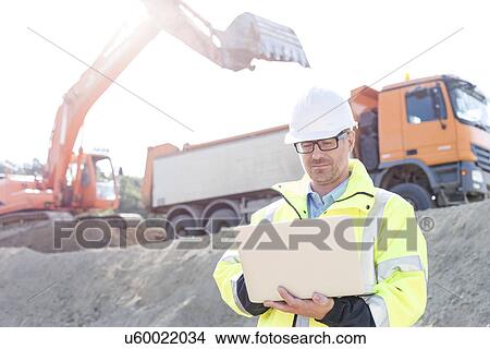 Picture - Supervisor using laptop at construction site on sunny day. Fotosearch