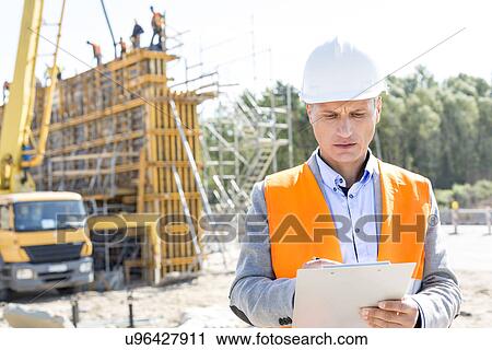 Stock Image - Supervisor writing on clipboard at construction site. Fotosearch