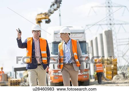 Stock Image - Supervisors discussing at construction site. Fotosearch