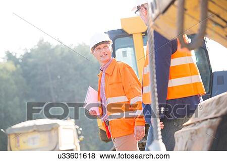 Stock Photo - Supervisors discussing at construction site on sunny day. Fotosearch