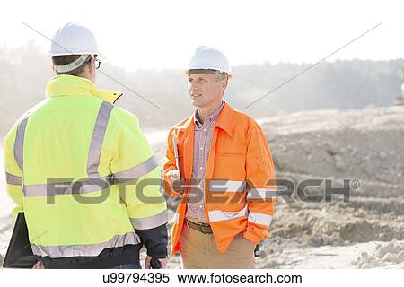 Stock Photography - Supervisors discussing at construction site on sunny day. Fotosearch