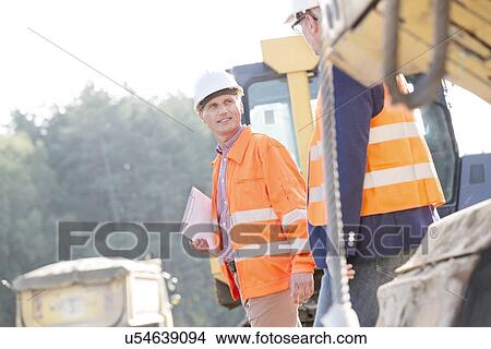 Supervisors discussing while walking at construction site View Large Photo Image Picture - Supervisors discussing while walking at construction site. Fotosearch