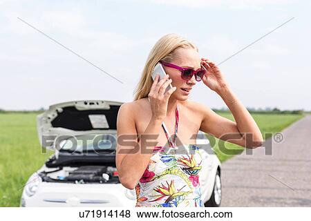 Tensed woman using cell phone on country road with broken down car in background View Large Photo Image Stock Photo - Tensed woman using cell phone on country road with broken down car in background. Fotosearch