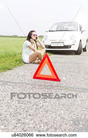 Tensed woman using cell phone while sitting by broken down car View Large Photo Image Stock Photograph - Tensed woman using cell phone while sitting by broken down car. Fotosearch