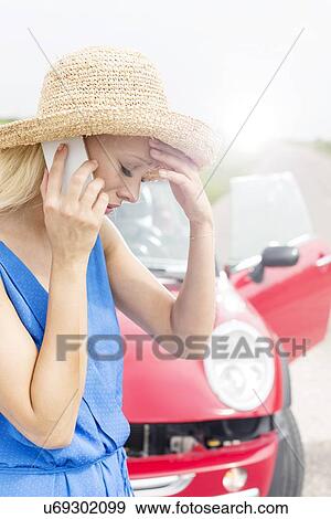 Stock Photo - Tensed young woman using cell phone by broken down car. Fotosearch