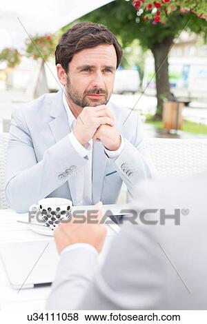Thoughtful businessman sitting with colleague at sidewalk cafe View Large Photo Image Stock Photo - Thoughtful businessman sitting with colleague at sidewalk cafe. Fotosearch