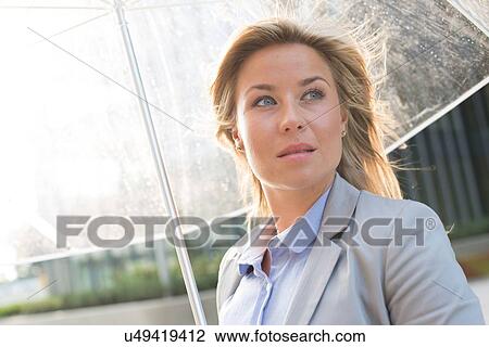 Stock Image - Thoughtful businesswoman with umbrella outdoors. Fotosearch