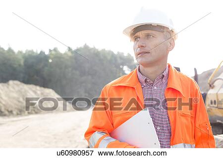 Stock Photo - Thoughtful engineer holding clipboard against clear sky. Fotosearch
