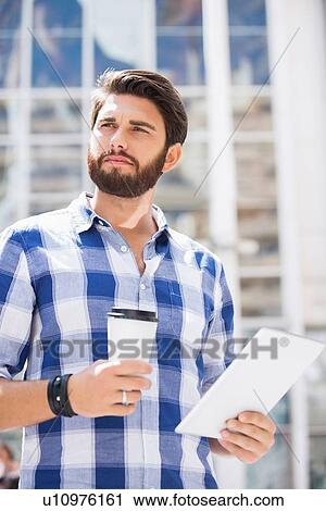 Thoughtful man looking away while holding disposable cup and tablet PC in city View Large Photo Image Stock Image - Thoughtful man looking away while holding disposable cup and tablet PC in city. Fotosearch