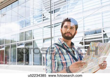 Thoughtful man looking away while holding road map against glass wall View Large Photo Image Stock Photography - Thoughtful man looking away while holding road map against glass wall. Fotosearch