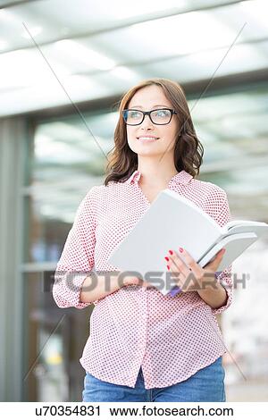 Thoughtful woman looking away while holding book outdoors View Large Photo Image Stock Image - Thoughtful woman looking away while holding book outdoors. Fotosearch