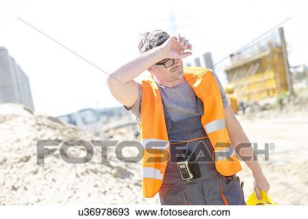 Tired construction worker wiping forehead at site View Large Photo Image Stock Image - Tired construction worker wiping forehead at site. Fotosearch