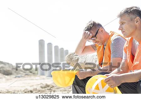 Tired supervisor sitting with colleague at construction site View Large Photo Image Stock Photography - Tired supervisor sitting with colleague at construction site. Fotosearch