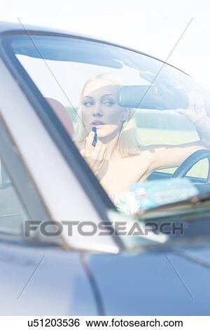 Woman applying lipstick in convertible on sunny day View Large Photo Image Stock Photograph - Woman applying lipstick in convertible on sunny day. Fotosearch