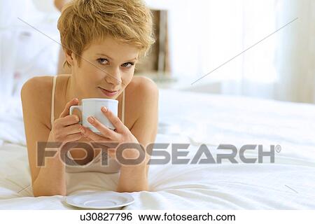 Stock Photograph - Woman drinking coffee in bed. Fotosearch