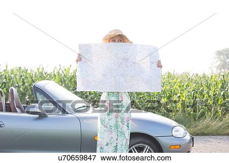 Stock Photo - Woman hiding face with map by convertible against clear sky. Fotosearch