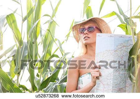 Stock Photo - Woman holding map while standing amidst plants outdoors. Fotosearch