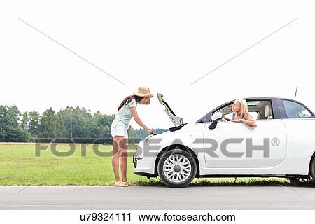 Woman looking at friend repairing broken down car on country road View Large Photo Image Stock Image - Woman looking at friend repairing broken down car on country road. Fotosearch
