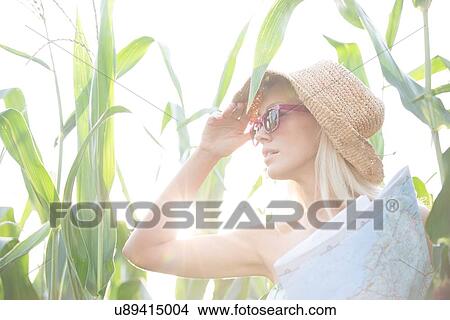 Picture - Woman looking away while holding map amidst plants on sunny day. Fotosearch