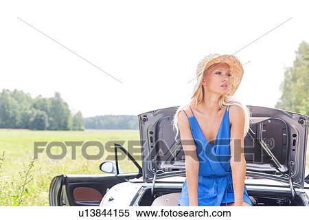 Woman looking away while sitting on convertible trunk against clear sky View Large Photo Image Stock Photography - Woman looking away while sitting on convertible trunk against clear sky. Fotosearch