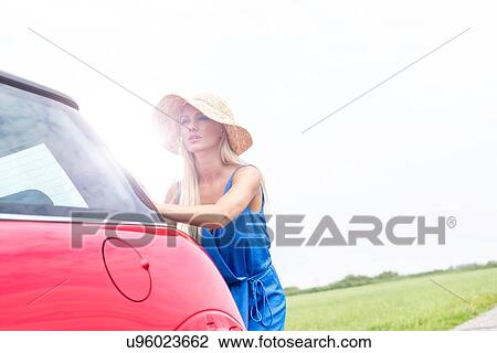 Stock Image - Woman pushing broken down car against clear sky. Fotosearch