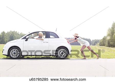 Stock Photography - Woman pushing broken down car on country road. Fotosearch