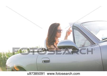 Stock Image - Woman reading map in convertible against clear sky on sunny day. Fotosearch
