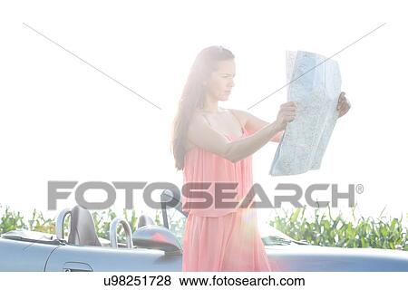 Stock Photo - Woman reading map while standing by convertible against clear sky. Fotosearch