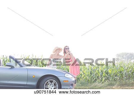 Picture - Woman showing something to female friend while reading map on convertible. Fotosearch