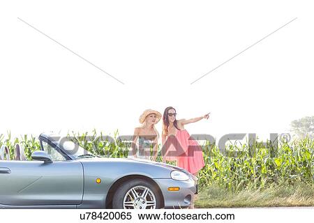Woman showing something to female friend while standing by convertible View Large Photo Image Stock Photography - Woman showing something to female friend while standing by convertible. Fotosearch