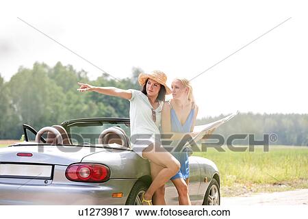Woman showing something to friend with map while leaning on convertible View Large Photo Image Stock Photo - Woman showing something to friend with map while leaning on convertible. Fotosearch