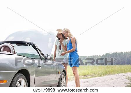 Women examining broken down car on sunny day against clear sky View Large Photo Image Stock Photo - Women examining broken down car on sunny day against clear sky. Fotosearch