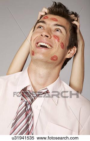 Stock Photography - Young caucasian businessman with lipstick kiss mark on his cheek. Fotosearch