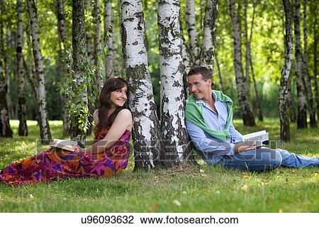 Young couple holding books in park by tree trunk, looking at each other View Large Photo Image Stock Image - Young couple holding books in park by tree trunk, looking at each other. Fotosearch